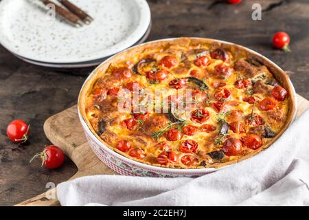 Quiche végétarienne tarte faite maison, avec des tomates cerises, aubergines et fromage feta sur un fond sombre. Banque D'Images