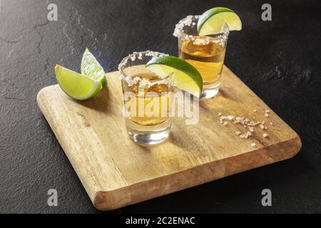 Tequila shots or avec lime slices et jantes de sel sur fond noir Banque D'Images