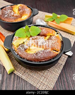 Klafouti tarte à la rhubarbe en noir brazier, menthe et rhubarbe tiges sur une serviette sur planche en bois historique Banque D'Images