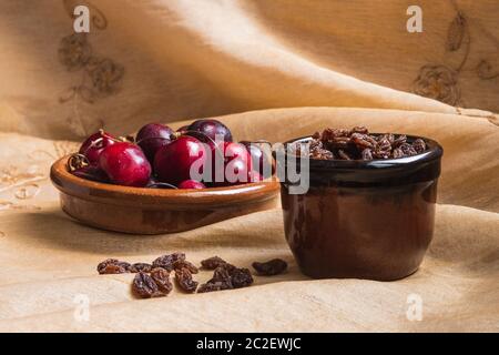 La vie de deux bols en céramique avec des cerises et des raisins secs sur une nappe dorée Banque D'Images