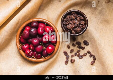 La vie de deux bols en céramique avec des cerises et des raisins secs sur une nappe dorée Banque D'Images