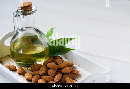 amandes en plaque blanche et bouteilles de verre avec huile sur une table en bois Banque D'Images