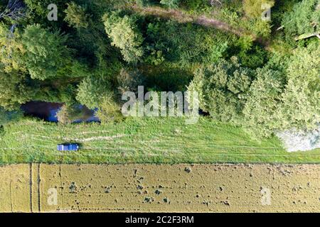 vue aérodynamique d'une voiture en voiture dans le pays entre une rivière, une forêt et un champ de blé vert Banque D'Images