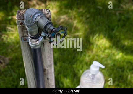 Robinet d'eau extérieur avec flacon de pompe d'assainisseur pour les mains sur le côté, vue rapprochée du dessus, mesures sanitaires Banque D'Images