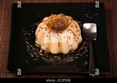 Le dessert sucré au lait de crème est servi sur une assiette carrée noire sur fond marron. Banque D'Images