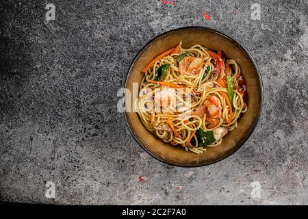 Incorporer les nouilles sautées avec les légumes et les crevettes dans un bol noir. Fond ardoise. Vue de dessus. Banque D'Images