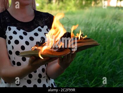 Livre brûlant dans les mains. Livres en feu dans la forêt. La jeune fille est titulaire d'un livre brûlant dans ses mains. Une jeune femme dans une forêt brûle un livre. Banque D'Images