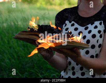 Livre brûlant dans les mains. Livres en feu dans la forêt. La jeune fille est titulaire d'un livre brûlant dans ses mains. Une jeune femme dans une forêt brûle un livre. Banque D'Images