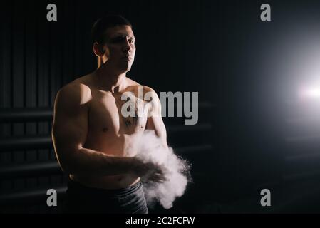 Homme musclé fort se clatant les mains avec le talc avant de soulever la barbell à la salle de gym. Banque D'Images