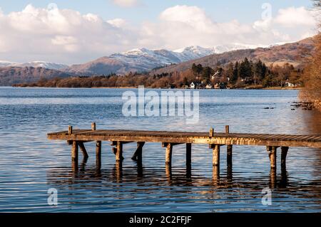 Le soleil d'hiver brille sur une petite jetée en bois du lac Windermere, sous les montagnes enneigées du parc national du Lake District d'Angleterre. Banque D'Images