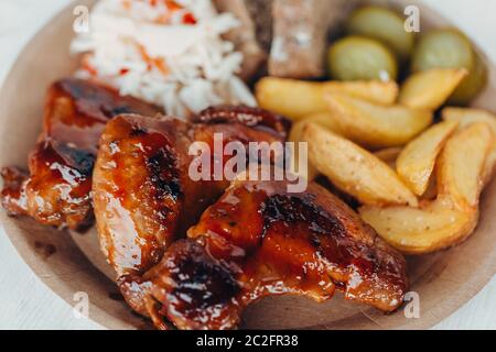 De délicieuses ailes de poulet frites avec sauce, pommes de terre frites, concombre, chou et khlobe dans une assiette en papier sur une table en bois Banque D'Images