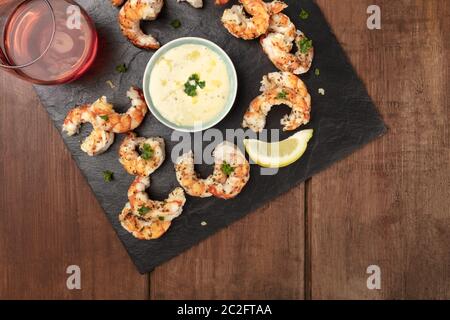 Crevettes frites avec une sauce César et un citron, prises d'en haut sur un fond rustique foncé en bois avec un verre de vin rose et de coco Banque D'Images