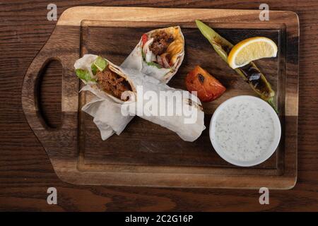 Roulé traditionnel turc et arabe Ramadan Adana kebab servant avec yaourt et poivre chaud isolé sur fond de bois Banque D'Images