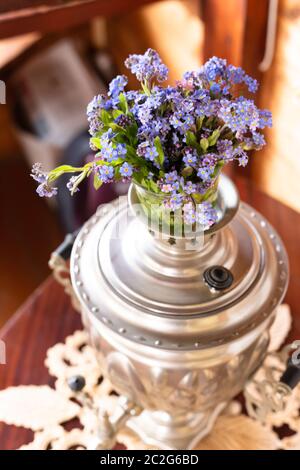 Vieux samovar en métal et un bouquet de fleurs bleues sur fond de bois Banque D'Images