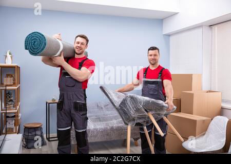 Portrait de deux jeunes Male Movers Carrying Rolled up Tapis et président d'enveloppement Banque D'Images