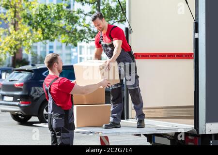 Deux jeunes hommes en uniforme les déménageurs transportant des boîtes de carton de chariot Banque D'Images