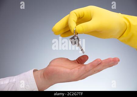 Close-up of a cleaner portant des gants jaunes clé remise sur la main de l'homme d'affaires contre l'arrière-plan gris Banque D'Images