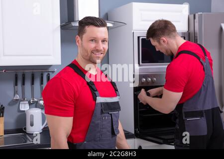 Jeune homme avec son assistant technicien en réparation du four dans la cuisine Banque D'Images