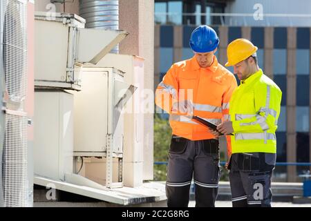 Deux électriciens hommes portant des vestes de sécurité Contrôle de l'unité de climatisation sur le toit du bâtiment Banque D'Images