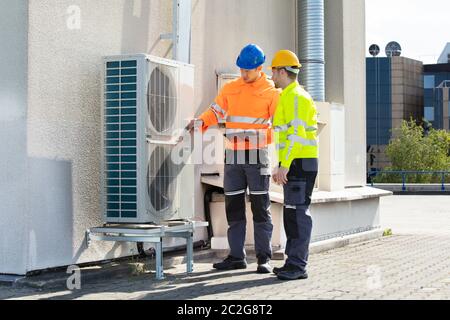 Deux électriciens hommes portant des vestes de sécurité Contrôle de l'unité de climatisation sur le toit du bâtiment Banque D'Images