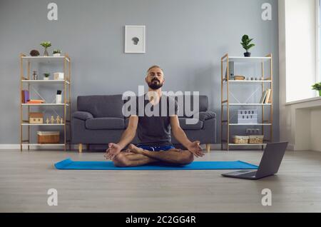 Cours de yoga en ligne. Un jeune homme paisible qui pratique la méditation du matin devant un ordinateur portable à la maison. Concept d'équilibre de vie Banque D'Images