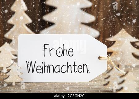 Une étiquette avec texte allemand Frohe Weihnachten signifie Joyeux Noël. Sapin de Noël en bois blanc comme décoration. Arrière-plan en bois brun avec neige Banque D'Images