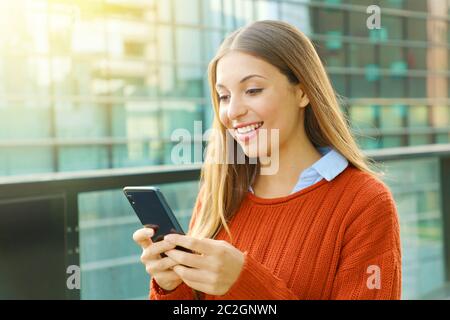 Young business woman texting on chandail orange le téléphone intelligent à l'extérieur du bureau dans une journée ensoleillée. Banque D'Images