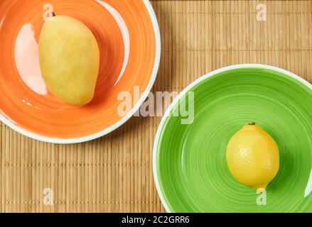 fruits jaunes - mangue sucrée sur une assiette d'orange et citron aigre sur une assiette verte - sur un tapis de service de canne Banque D'Images