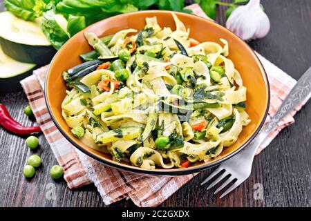 Tagliatelles aux courgettes, petits pois, haricots asperges, poivrons et les épinards dans une serviette de cuisine, l'ail, basilic et fourche sur planche de bois background Banque D'Images