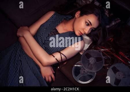 Portrait d'une jeune fille asiatique dans une robe rayée bleu couché sur la table à côté des bobines avec bande magnétique Banque D'Images