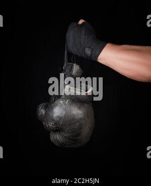 Le bras de l'homme enveloppé dans un bandage élastique noir sports détient old vintage paire de gants de boxe en cuir, fond noir Banque D'Images