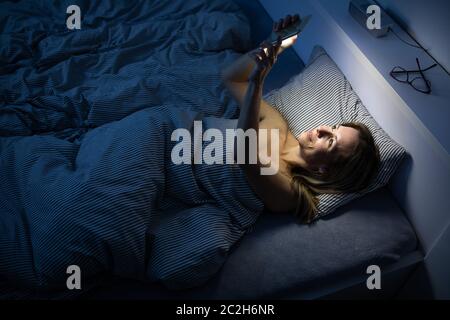 Jolie femme d'âge moyen, en utilisant son téléphone portable au lit à la maison avant de dormir Banque D'Images