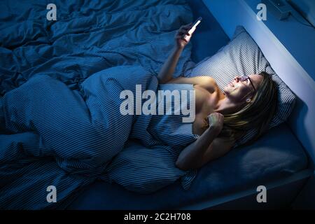 Jolie femme d'âge moyen, en utilisant son téléphone portable au lit à la maison avant de dormir Banque D'Images