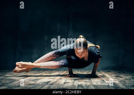 Jeune femme pratiquant le yoga faisant huit-angle poser asana dans la pièce sombre Banque D'Images