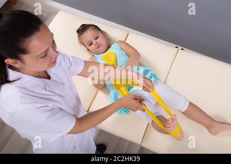 Une vue de dessus d'un physiothérapeute qui s'étend de la jambe sur le lit de fille à l'hôpital Banque D'Images