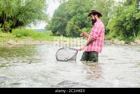 Pêche à la baissière. Pêcheur barbu dans l'eau. Activités de loisir et de sport. Pothunter. Week-end d'été. Pêche au gros gibier. Pêcheur avec canne à pêche. Homme mature pêche à la mouche. Homme attrapant le poisson. Banque D'Images