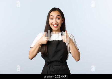 Café-restaurant, petite entreprise et concept de démarrage. Une serveuse asiatique souriante et enthousiaste approuve un nouveau menu. Le barista mignon en tablier noir se montre bien Banque D'Images