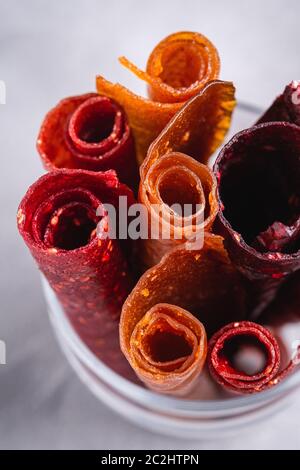 Pastille de fruits dans une tasse de verre sur fond de béton de pierre. Nourriture roulait sans sucre biologique à base de framboise, fraise, pêche et pomme. Maison végétalienne Banque D'Images