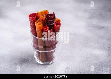 Pastille de fruits dans une tasse de verre sur fond de béton de pierre. Nourriture roulait sans sucre biologique à base de framboise, fraise, pêche et pomme. Maison végétalienne Banque D'Images