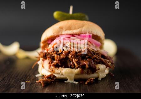 Porc lentement cuit tiré avec sauce barbecue, oignons marinés, coleslaw et fromage servis dans un pain hamburger avec cornichon d'aneth et frites en tant que côtés. C'est désordonné. Banque D'Images