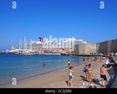 touristes sur la plage près du port de la ville de rhodes avec le bateau de croisière carnival vista amarré derrière le fort Banque D'Images