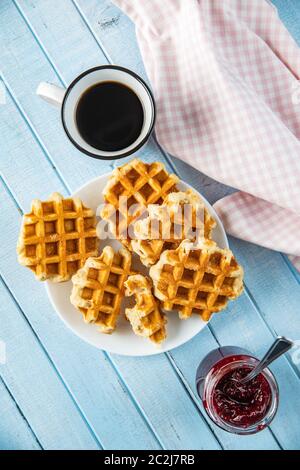 Gaufres sucrées savoureux avec confiture de framboises et tasse de thé sur la table bleue. Vue d'en haut. Banque D'Images