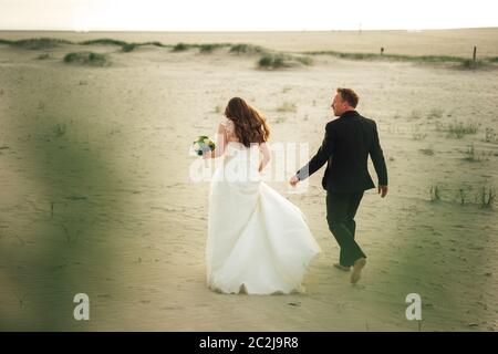 Couple de mariage marchant sur une plage de sable. Vue arrière des mariés. Mari pieds nus. Concept de mariage. Banque D'Images