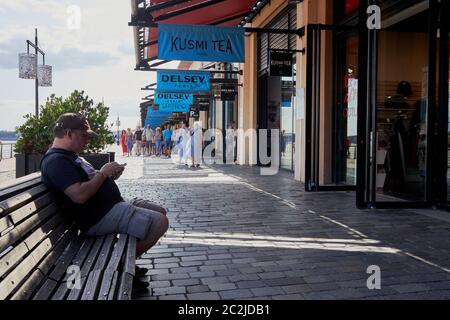 Un homme en casquette et short de baseball assis utilise son téléphone mobile dans le quartier de vente au détail au bord de la rivière appelé Quai des marques (quai de marque) Bordeaux, France Banque D'Images