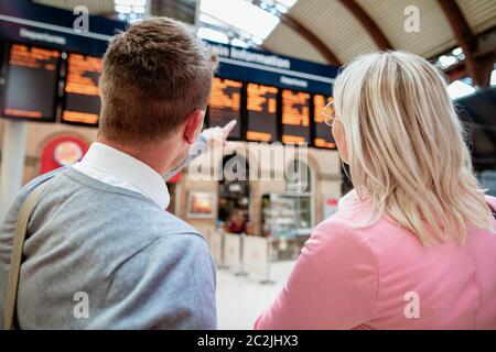 Un businessman and businesswoman looking at a departure board dans une gare. Banque D'Images