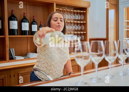 Un membre du personnel verse du vin blanc dans une rangée de verres au bar de dégustation du Château Lagrange, verres suspendus, Saint-Julien, Bordeaux, France Banque D'Images