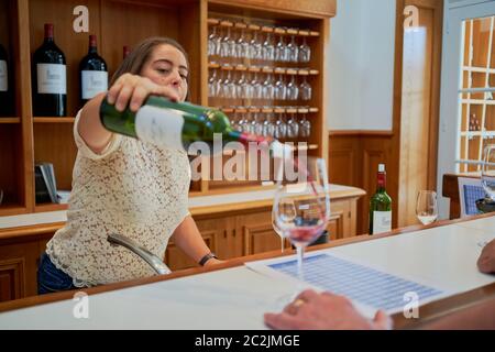 Un membre du personnel sert du vin rouge à un client au comptoir de dégustation de Chateau Lagrange, bouteilles de l'exploitation et verres suspendus, Saint-Julien, France Banque D'Images