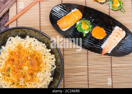 Des sushis et des plats de nouilles en noir sur fond de bois Banque D'Images