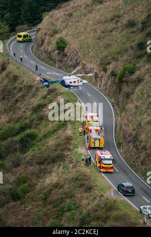 Un hélicoptère de sauvetage MB BK117 / H145 déchaîne d'une route sur le côté d'une montagne à côté des véhicules de service d'urgence Banque D'Images