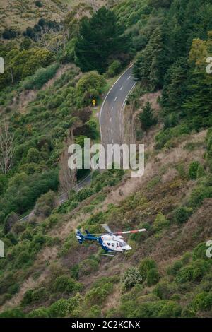 Un hélicoptère de sauvetage BK117 / H145 récupère le conducteur d'un véhicule qui a quitté la route et est tombé sur une pente abrupte couverte de brousse à Christchurch, en Nouvelle-Zélande Banque D'Images